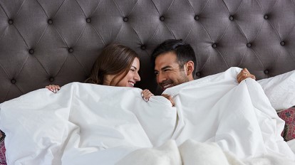 Sweet couple in bed under a white blanket smiling at each other