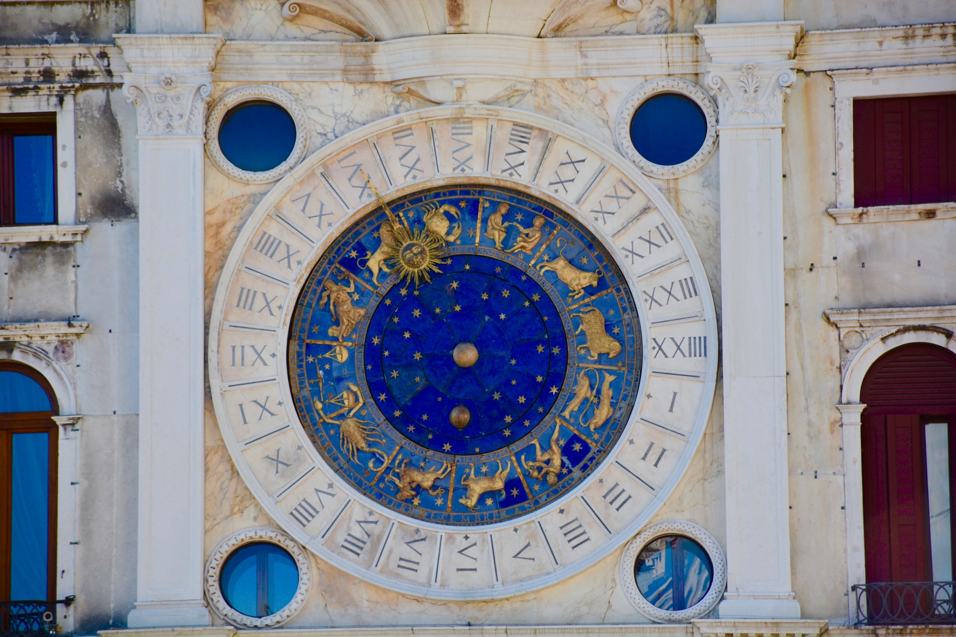 Blue Astrology clock with gold symbols made in stone on a white building 