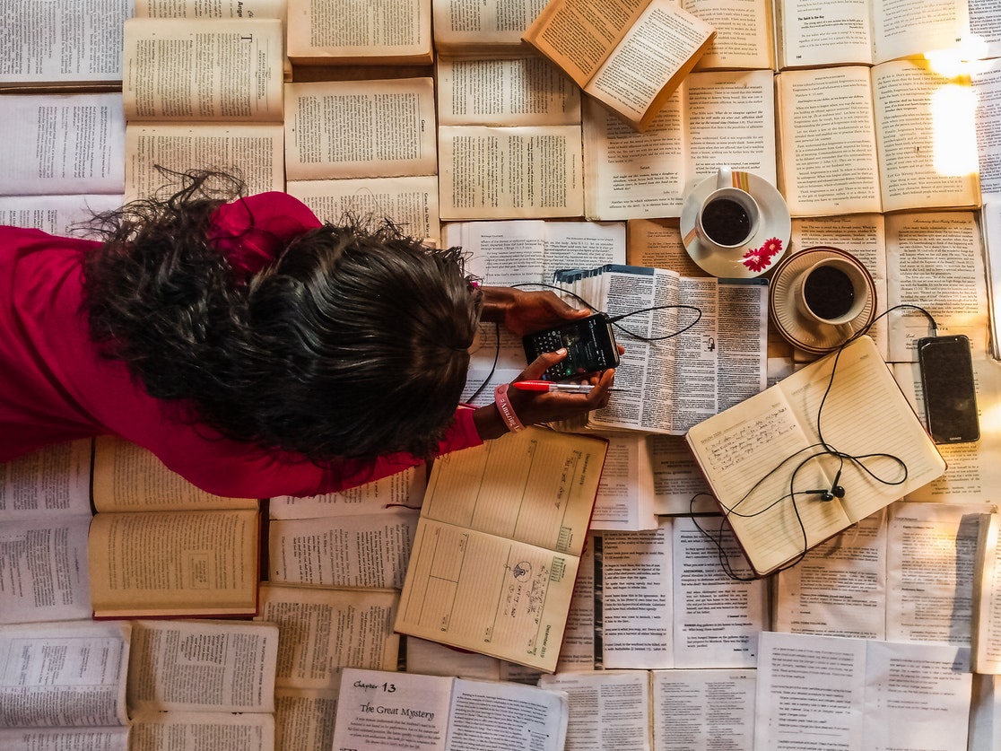 Overhead Shot of a Woman Using a Mobile Phone lying on top of open books and notebooks and 2 cups of coffee