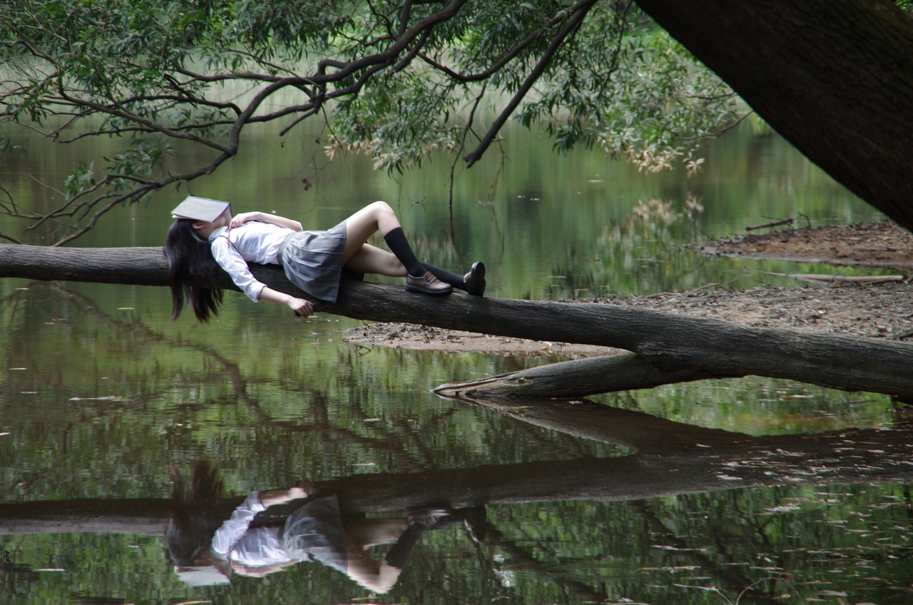 Woman Lying on Tree above the lake with a book on her face