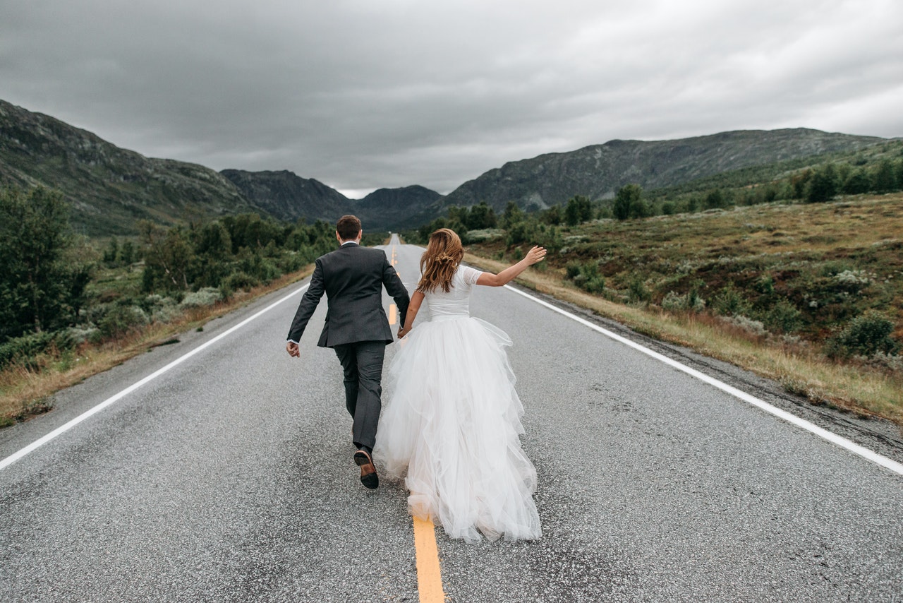 Back View of a Groom and a Bride Running in the Middle of a Road