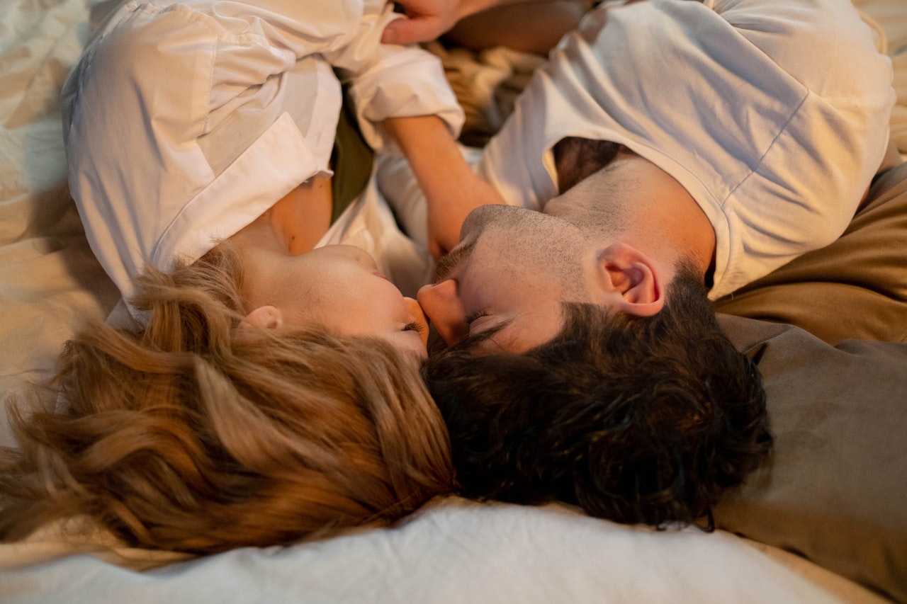 A Couple lying in bed with their heads close to each other and eyes closed