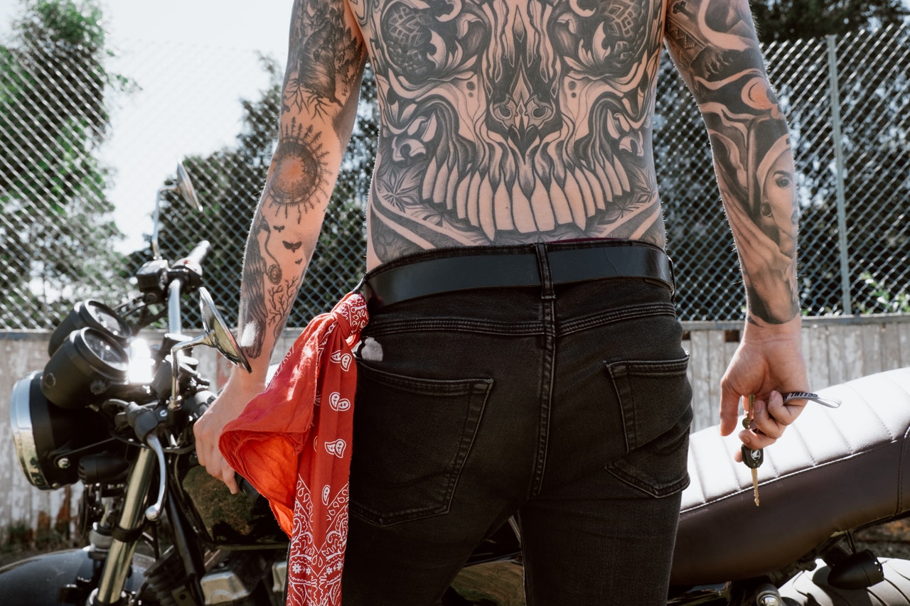 A Shirtless Tattoo Person Holding a Key in Front of a Motorbike