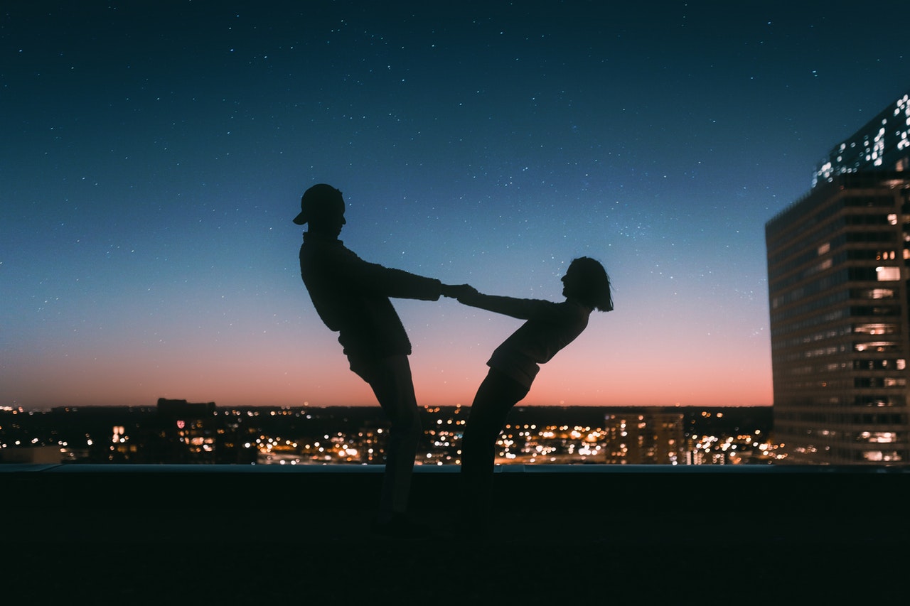 Silhouette of Man holding a womans hands on top of a building while dancing