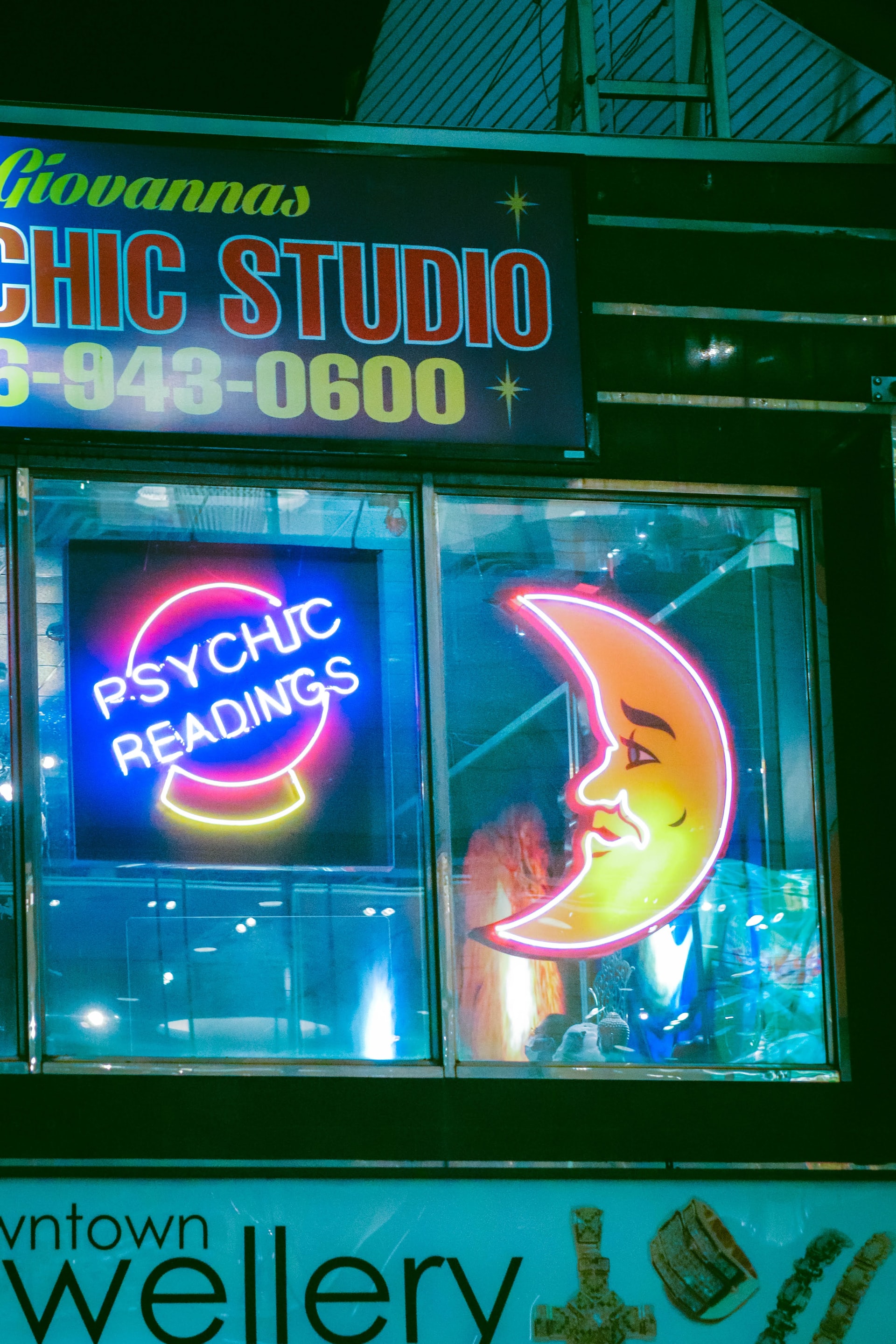 Crescent moon neon sign with another neon sign that reads psychic readings and the name and number of the studio