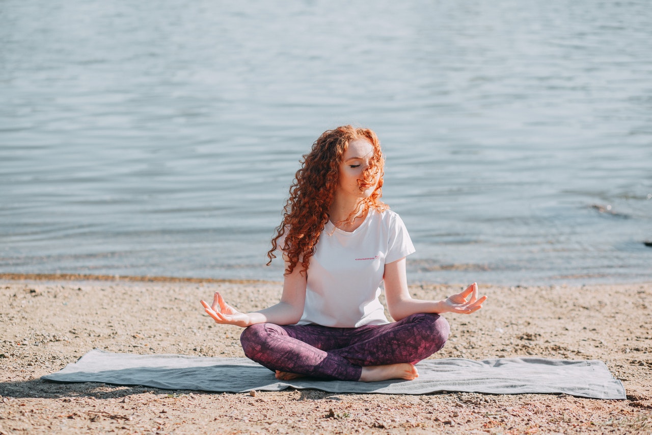Woman with curly red hair Doing Yoga Exercise At The Sea Shore