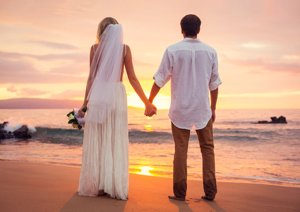 A man and woman wearing wedding clothes holding hands and staring at the sea