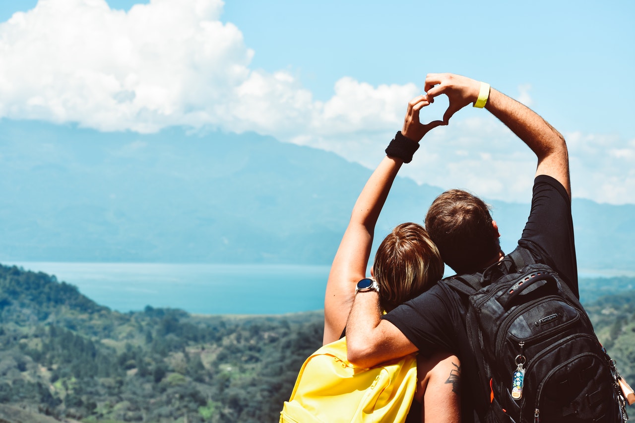 Two People Forming Heart Hand Shape with overlooking lake and mountains