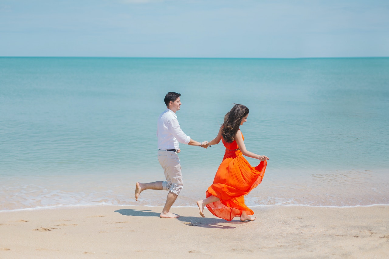 Man wearing white shirt and Woman wearing orange dress running on shore