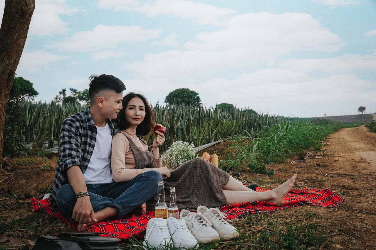 Man And Woman Sitting On Red Textile Having A Picnic both took off their shoes