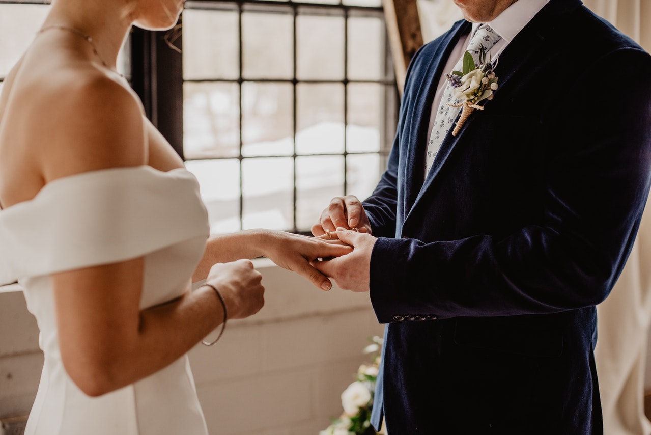 Man putting a ring on his bride's hands on their wedding