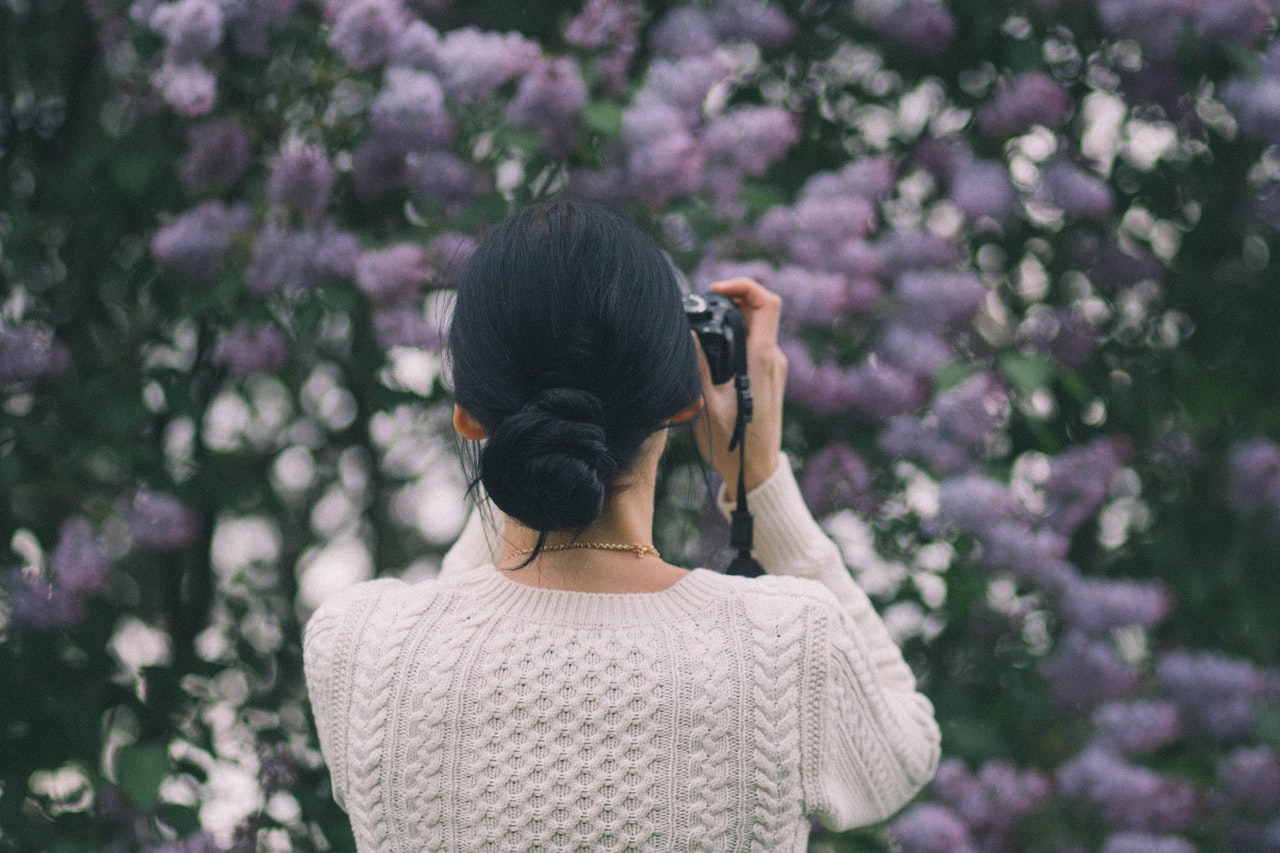 Woman Holding Camera while Taking Photos of Flowers