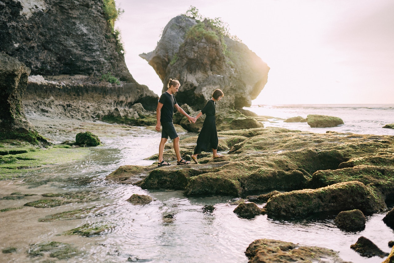 A Couple Walking on Rocks in the Beach Shore both wearing black