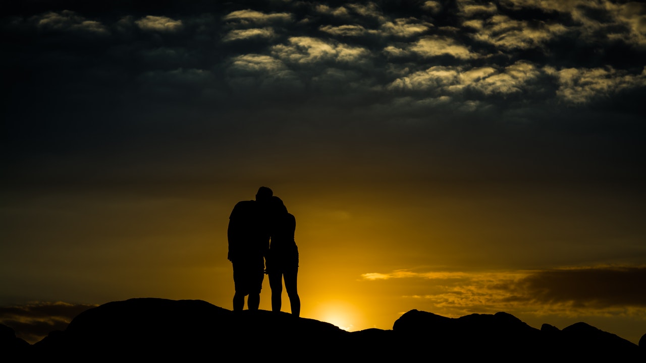 Man and Woman standing over rock during sunset