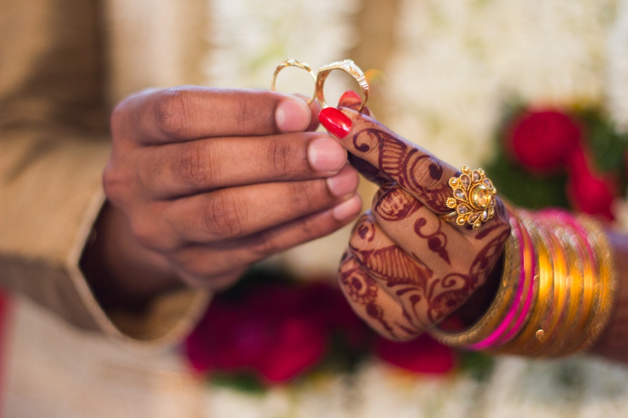 Man and Woman's left hand covvered with tattoos and wearing a ring ang gold bangles Holding Wedding Rings