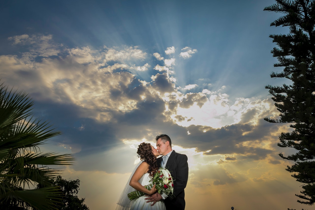 Couple Kissing Each other with sunlight going through clouds behind them and trees on the side