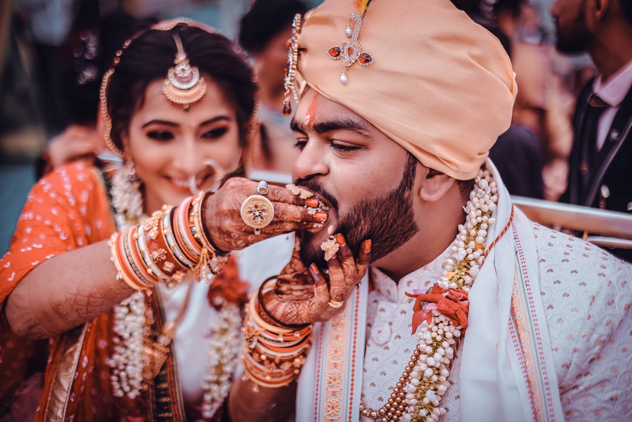 Woman with Mehndi Patterns and Jewelry Feeding Bearded Man in White Clothes and Turban