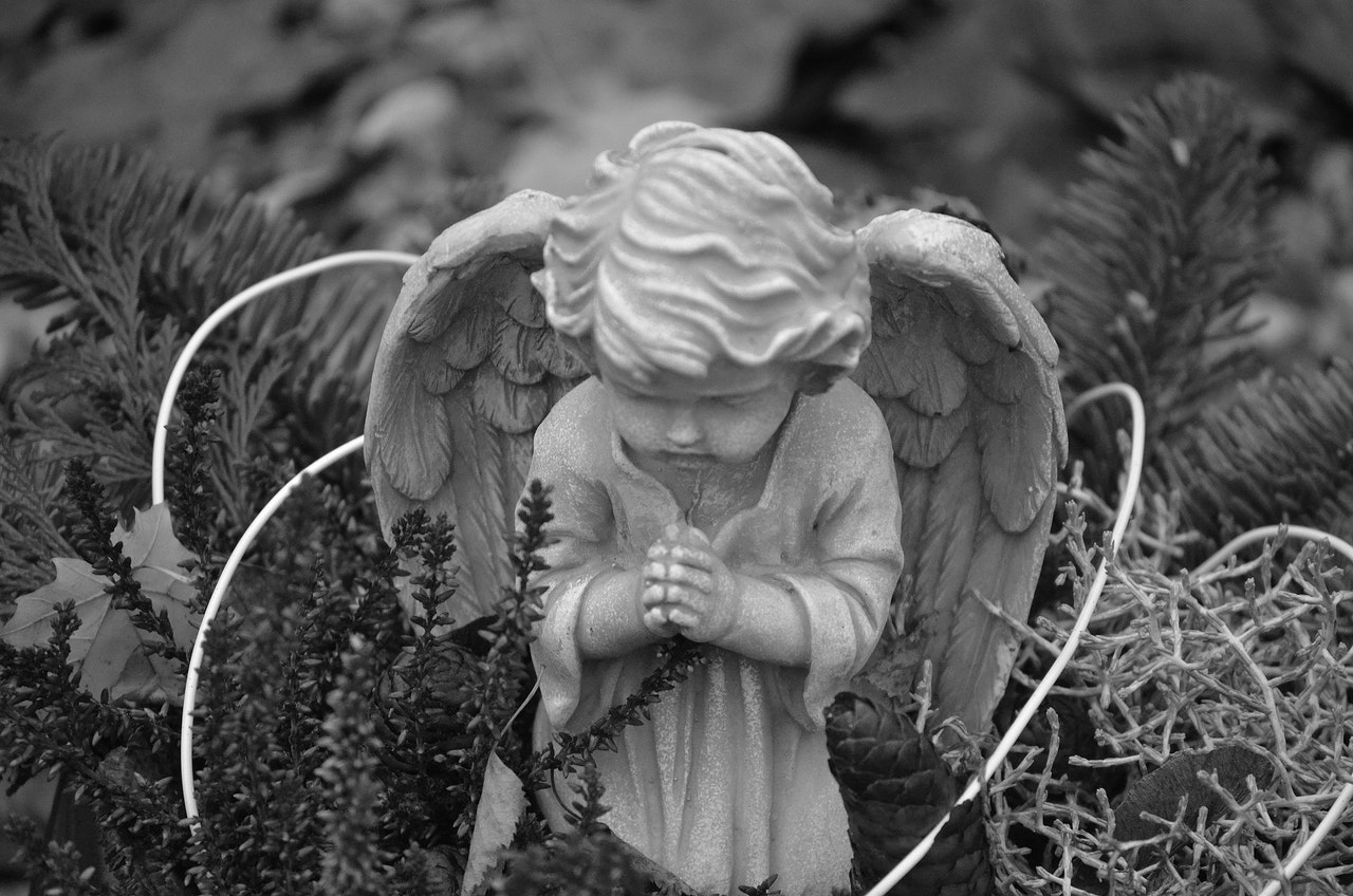Grayscale photo of a marble statue of a praying angel