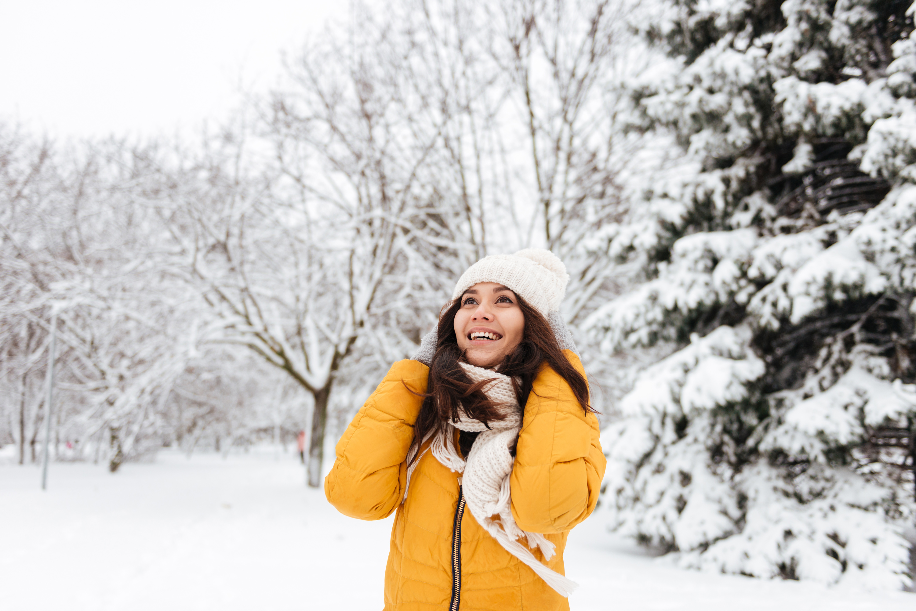 A girl in yellow jacket and white hat smiling in snow