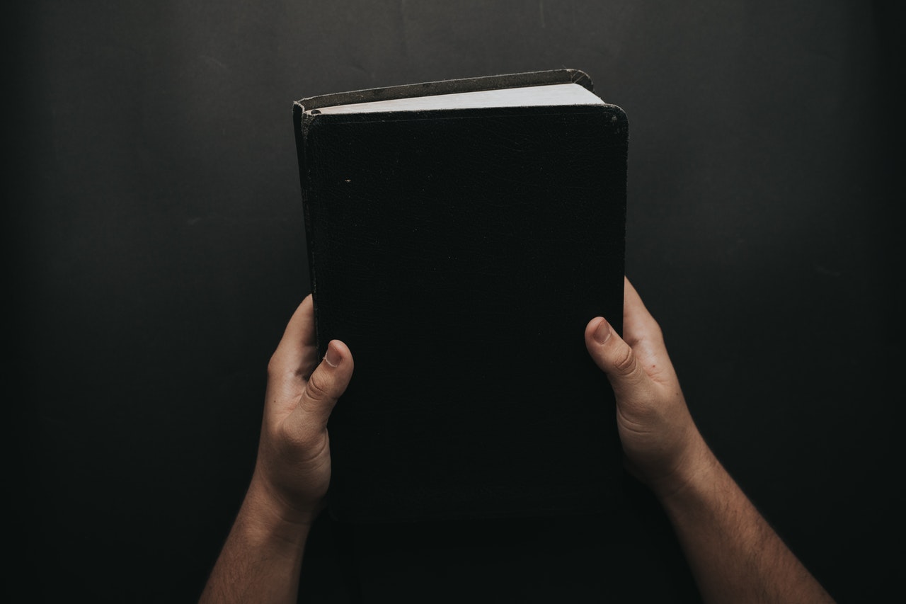 Person Holding A Black Bible