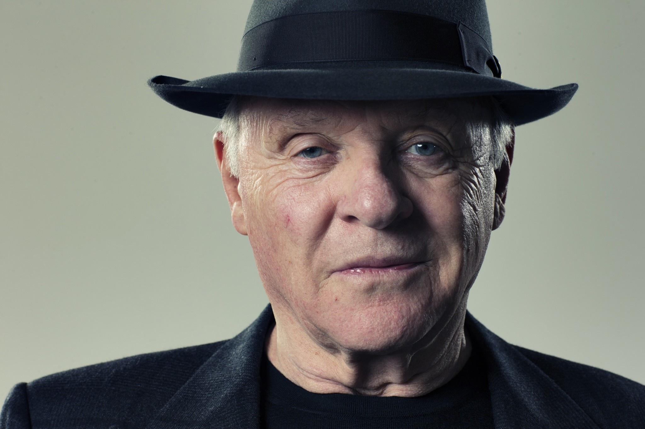 Anthony Hopkins wearing a black shirt and hat while smiling