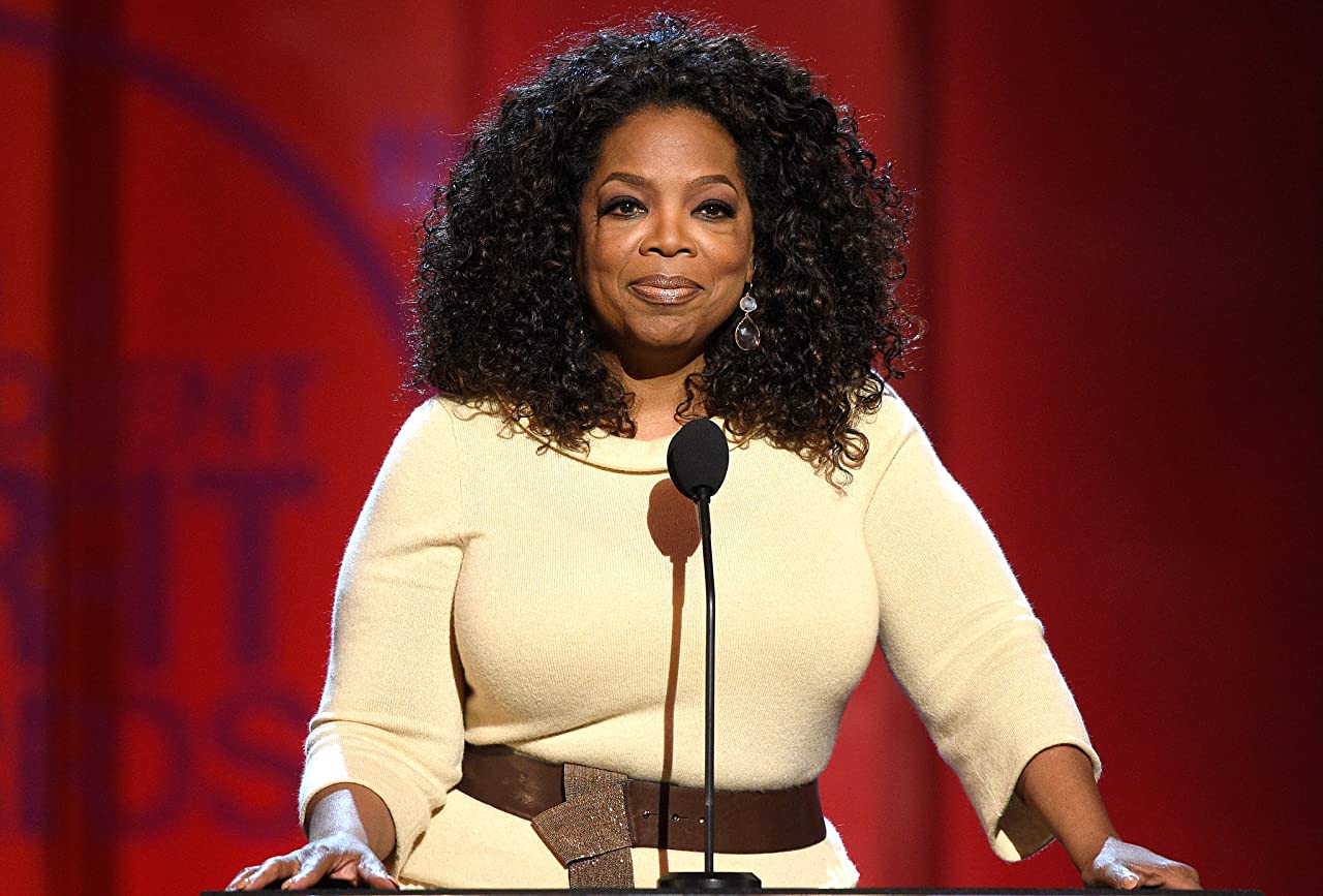 Oprah Winfrey smiling while in front of a microphone and podium