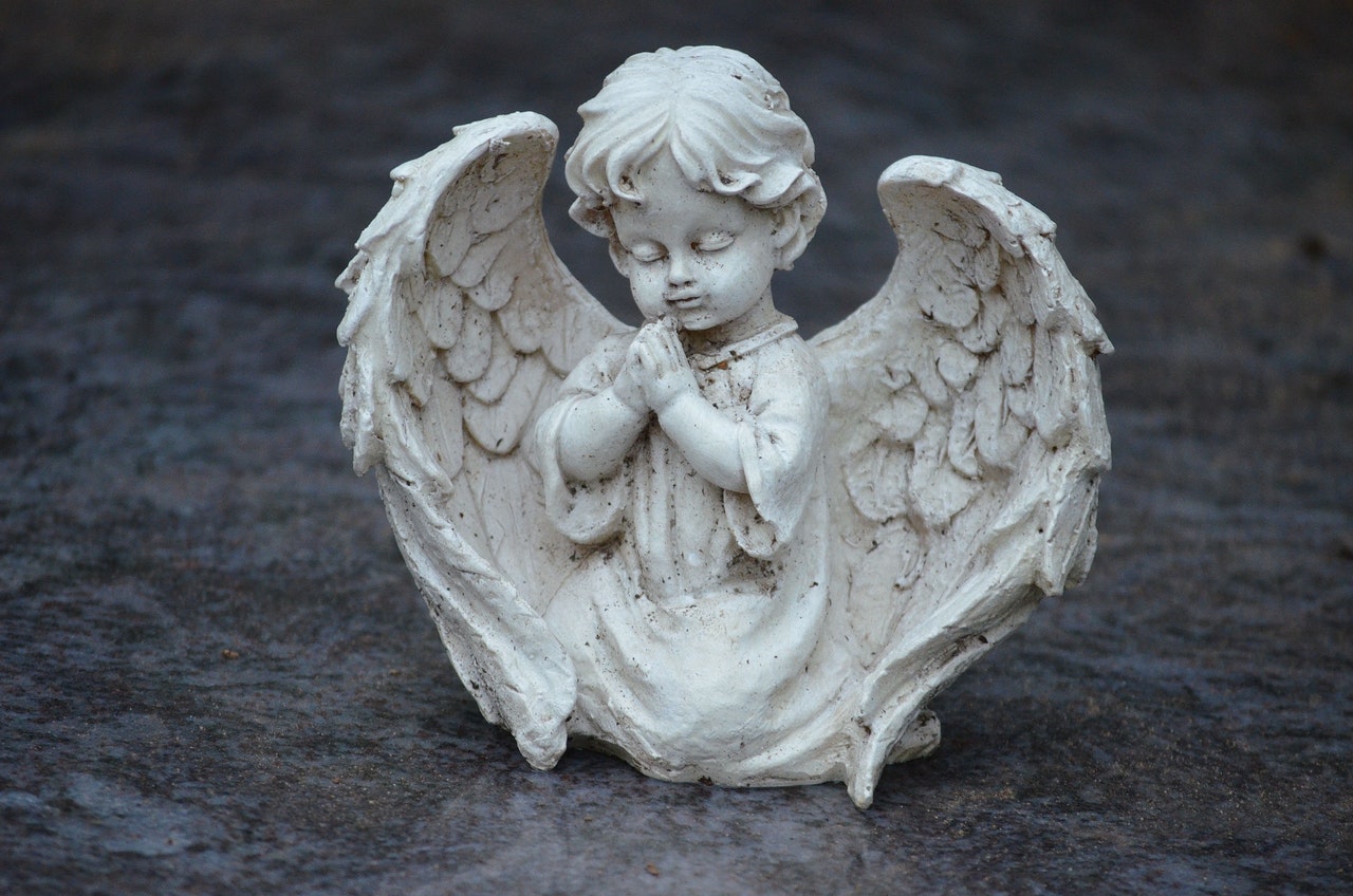 An Angel Figurine Kneeling On The Ground While Praying