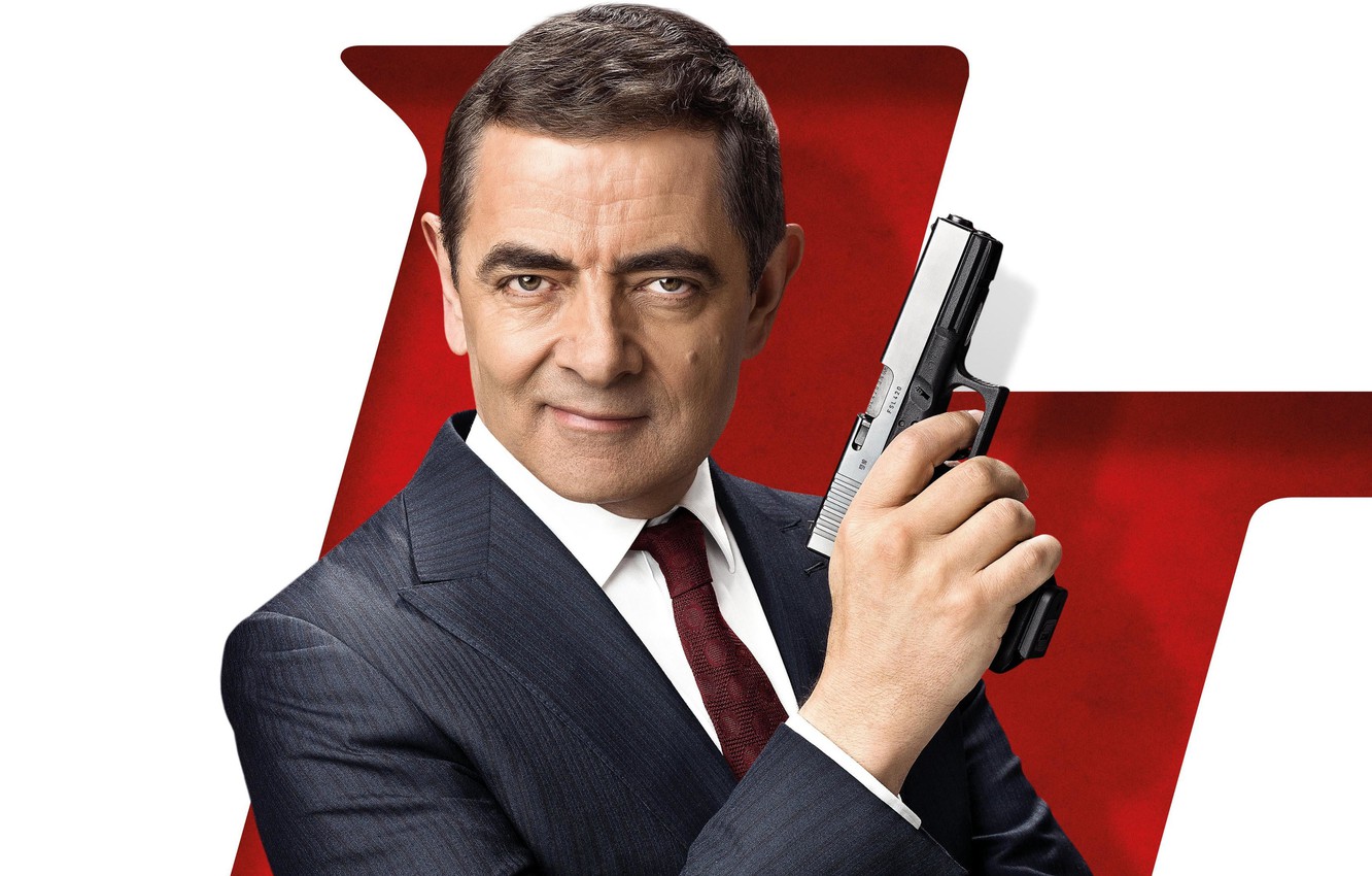 Rowan Atkinson smiling while holding a gun on his right hand