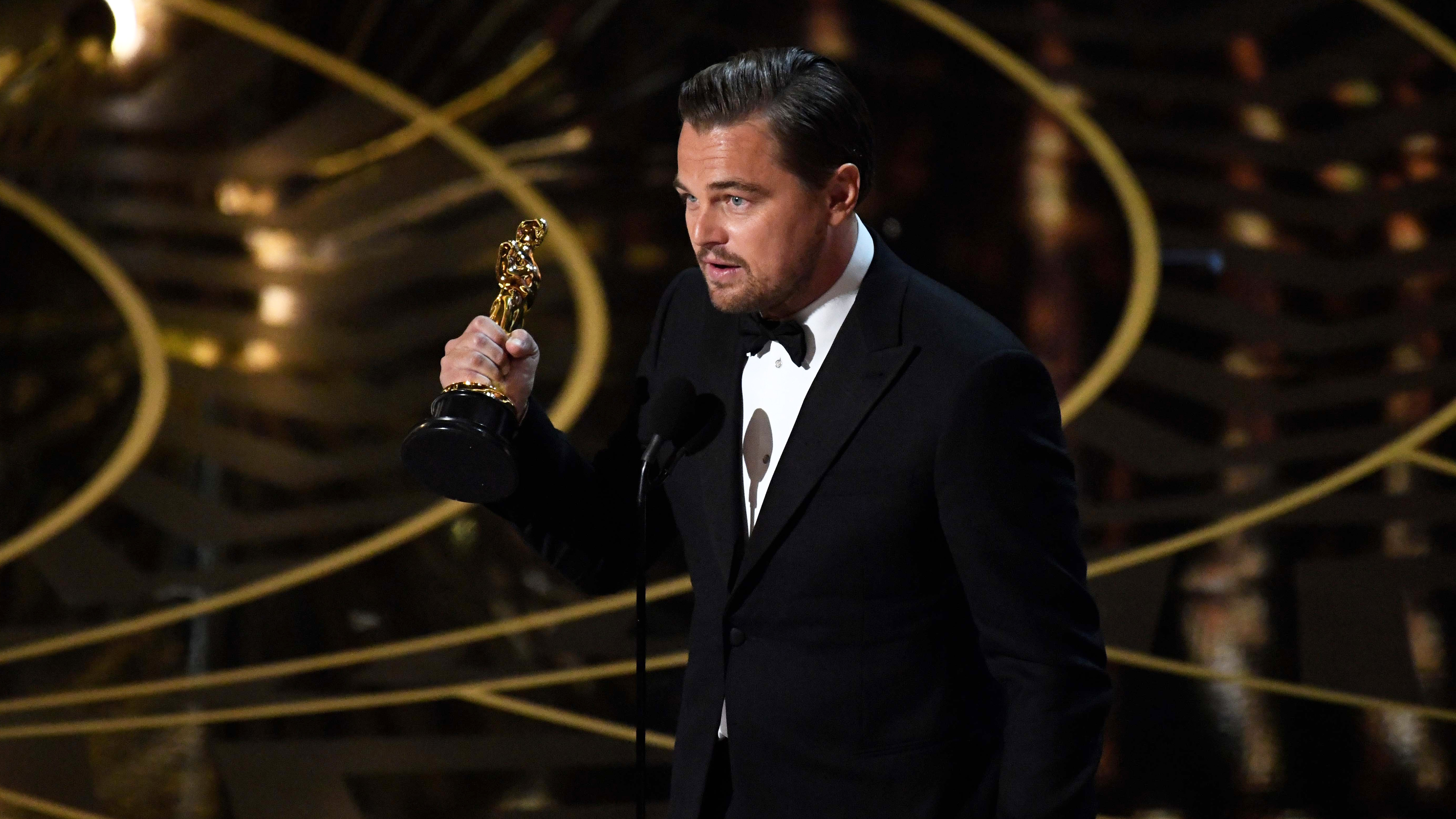 Leonardo DiCaprio holding a trophy while speaking on a microphone