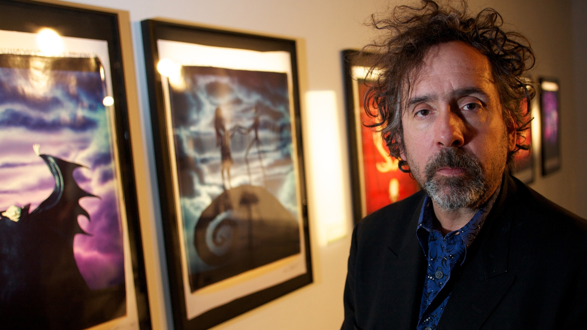 Tim Burton with messy hair and some paintings on his back