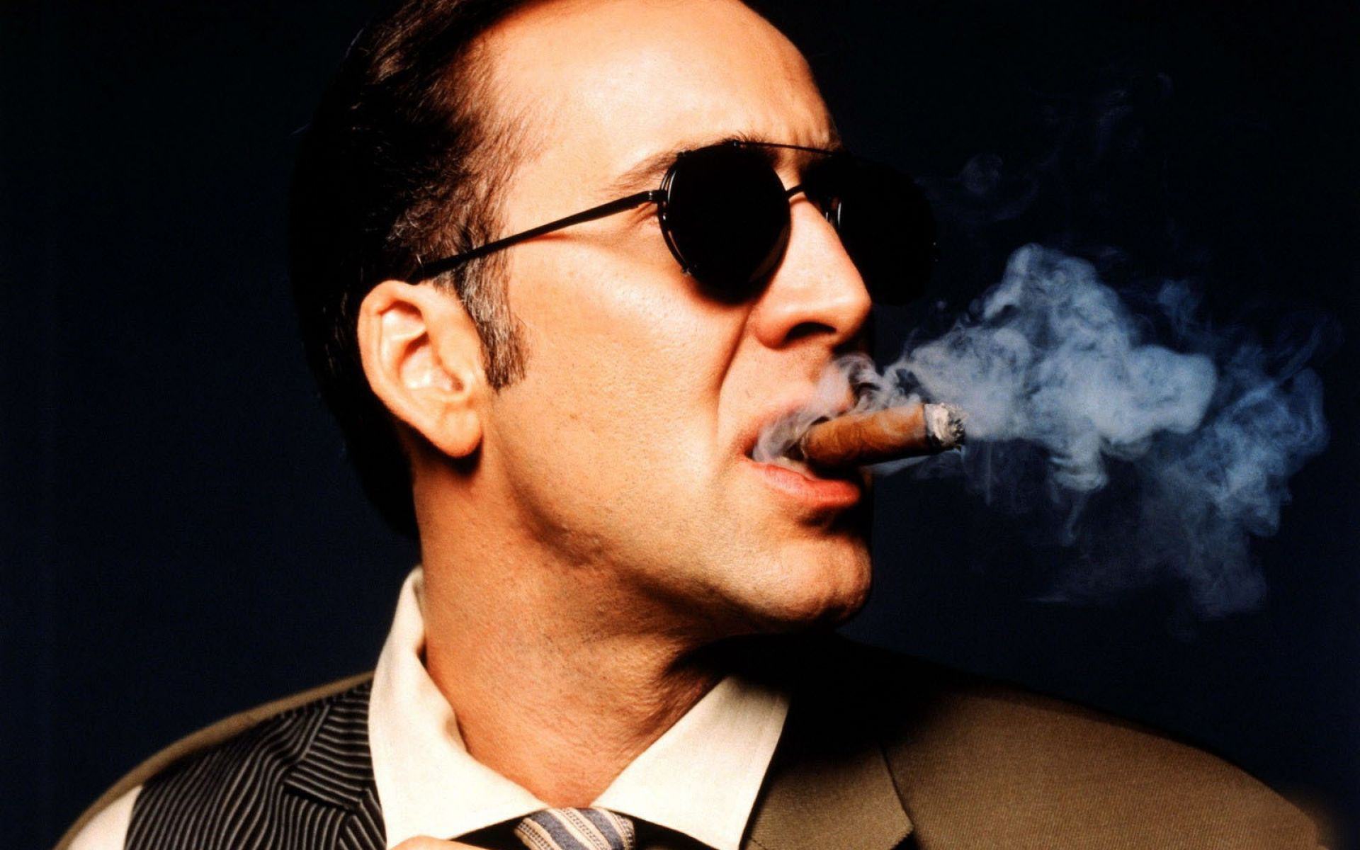 Nicolas Cage wearing sunglasses and smoking a tobacco