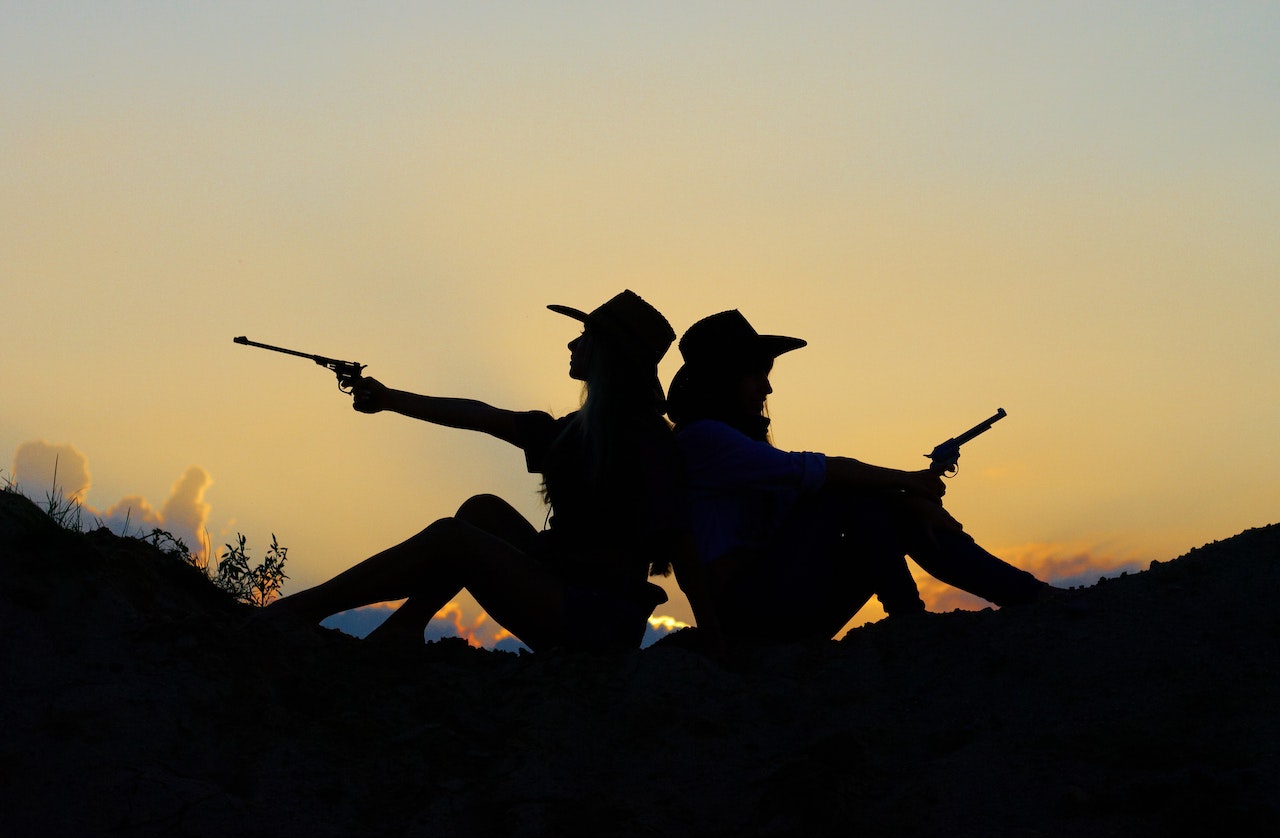 Silhouette of Two People Holding Revolver Pistols Sitting on the Hill