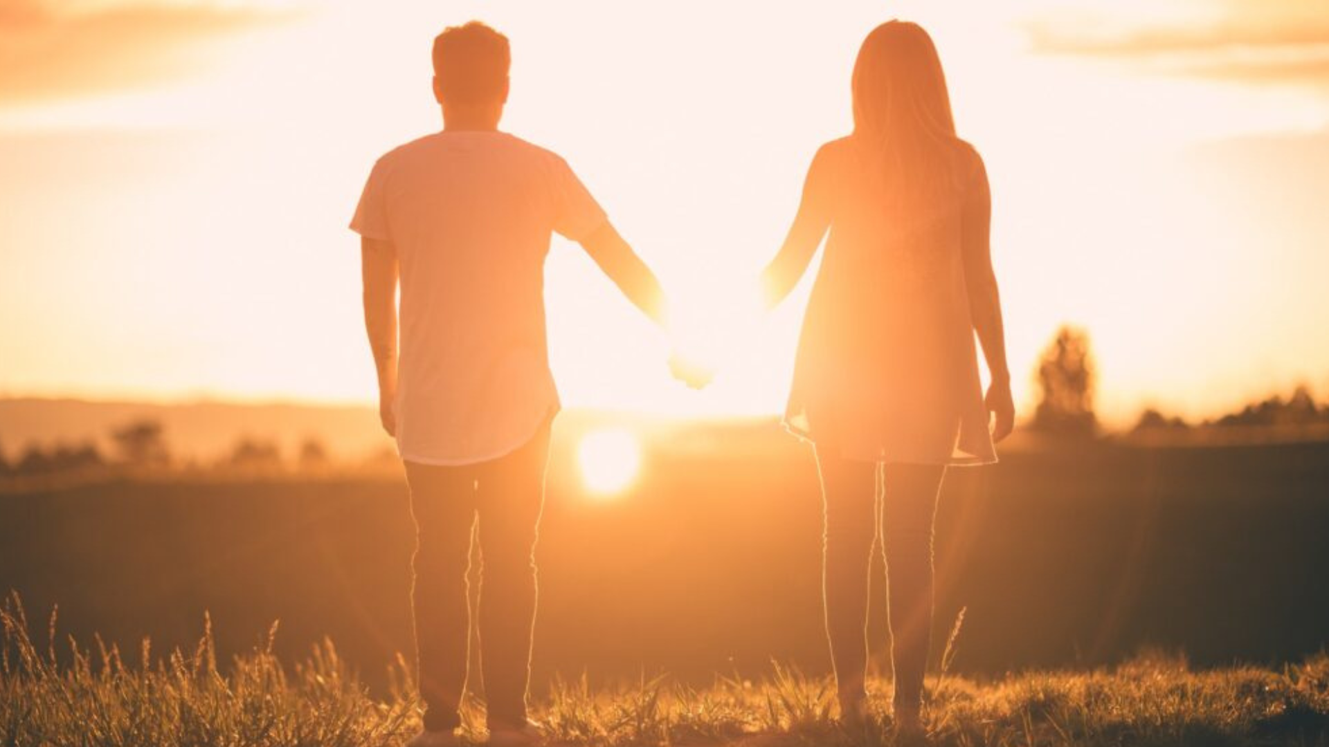 Two people holding their hands while standing and looking at the sunset