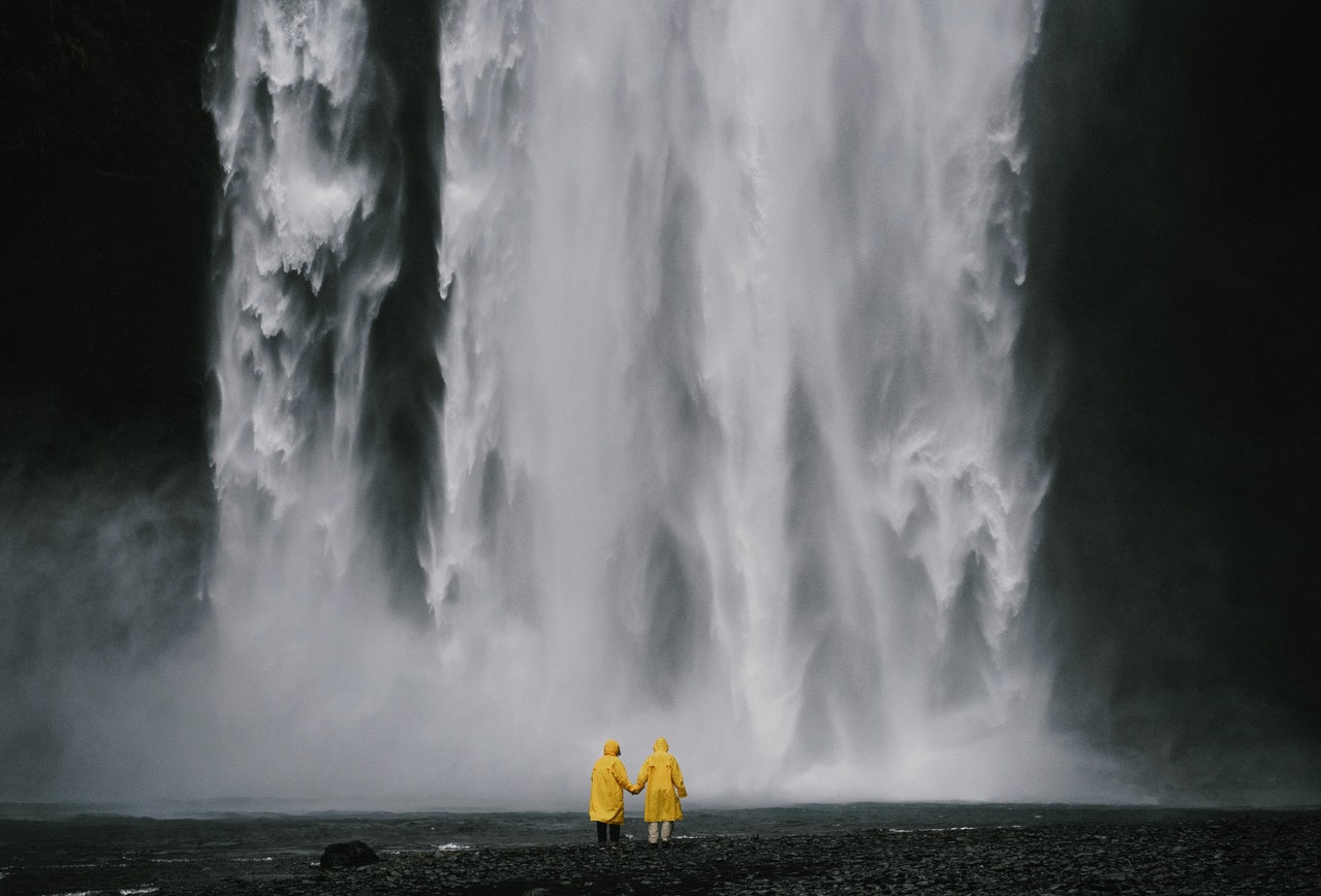Travelers in yellow coats holding hands in front of the spectacular waterfall