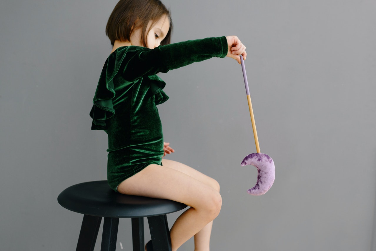 A Young Girl in Green Bodysuit Sitting on the Chair while Holding Moon Wand