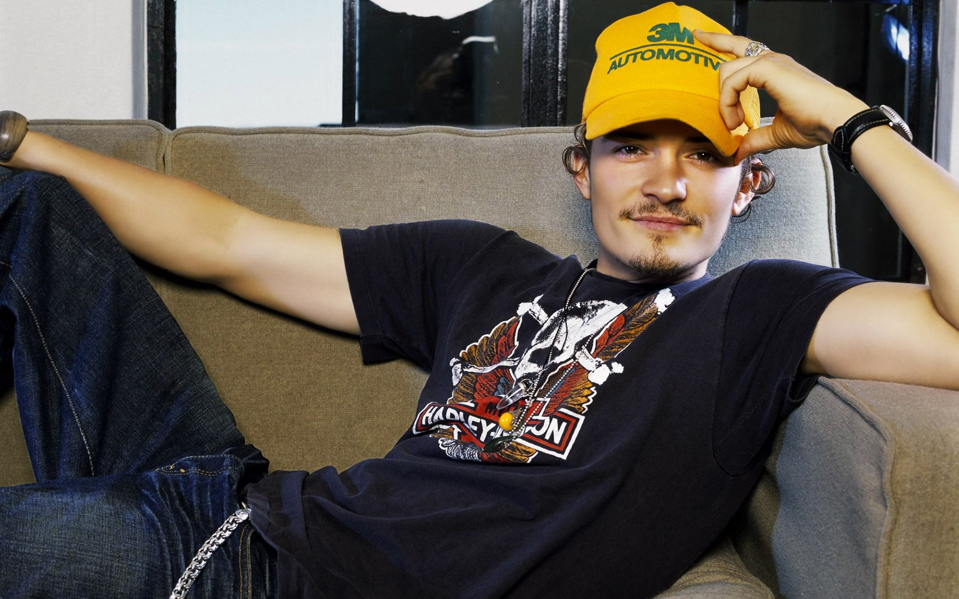 Orlando Bloom wearing a yellow cap while lying on the couch