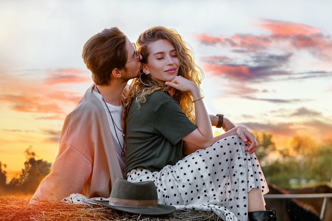 Man kissing attractive girlfriend on haystack at sunset