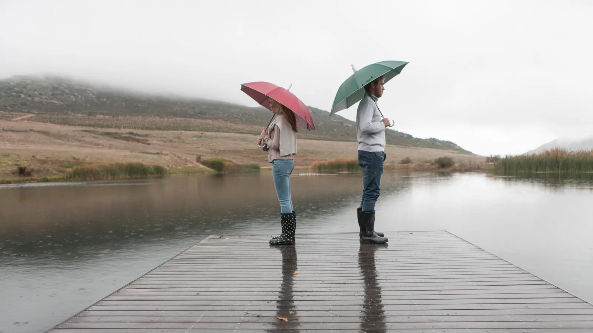 Two people holding an umbrella and facing against each other