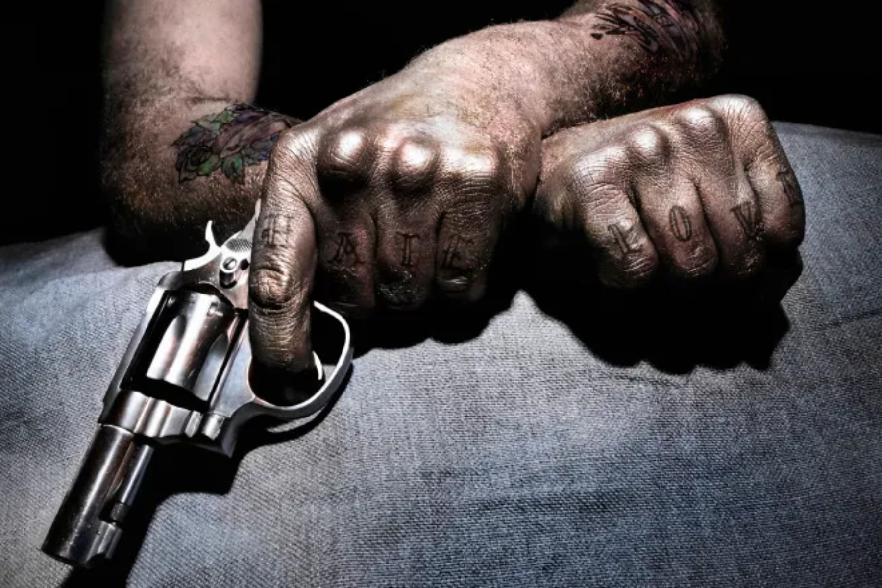 A tattooed man with a pistol crosses his arm