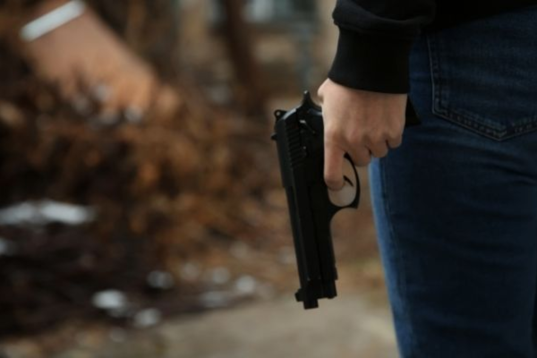 A man in jeans and a black jacket holds a gun and points it downward