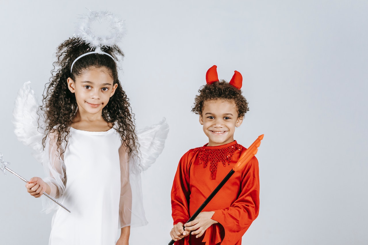 Cute children in angel and devil costumes smiling at camera in white studio