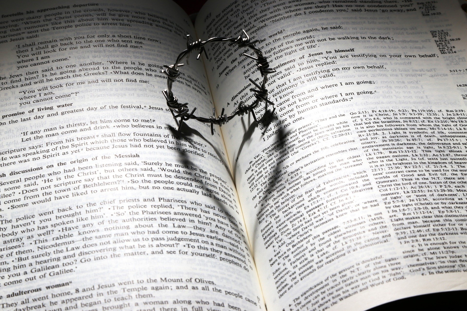 An open Bible with a metal wire on top of it forming a heart-shaped shadow