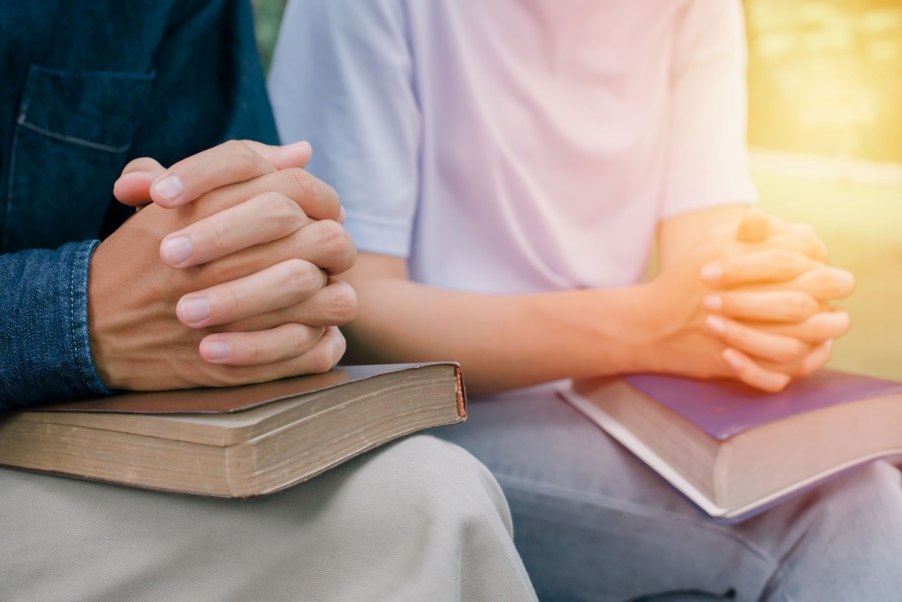 2 persons with hands together on top of Bibles