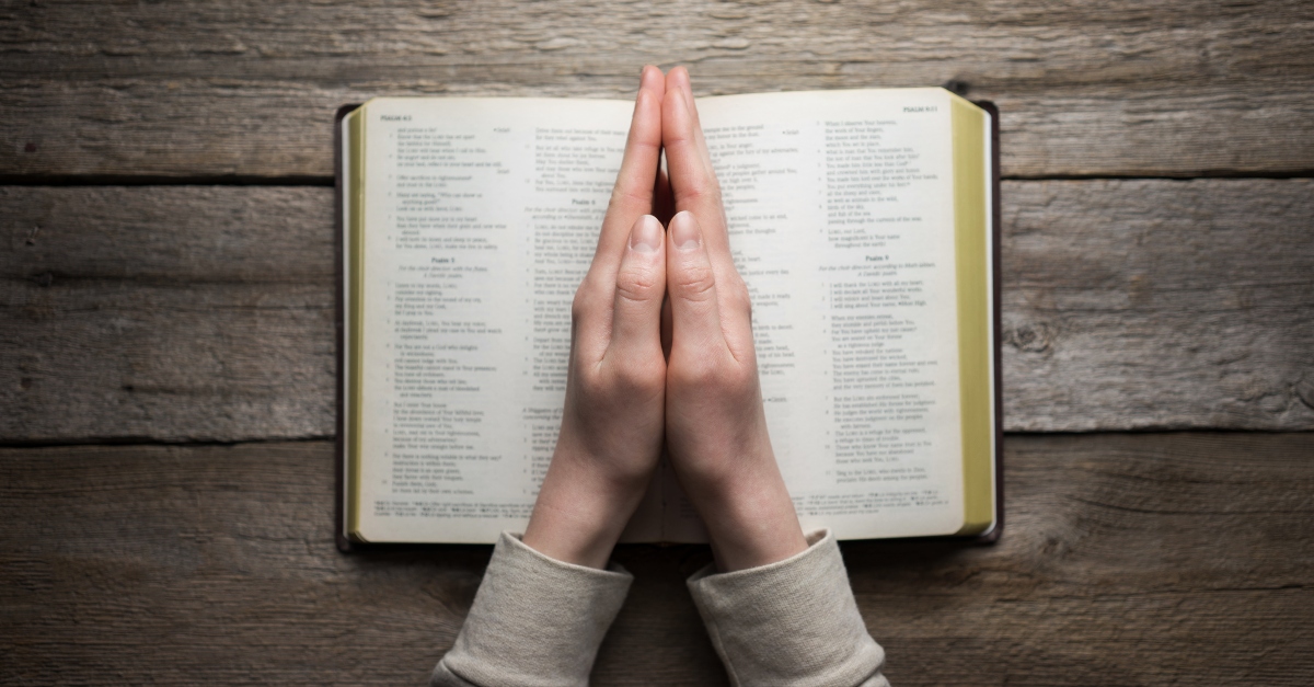 Hands in a praying position on a Bible