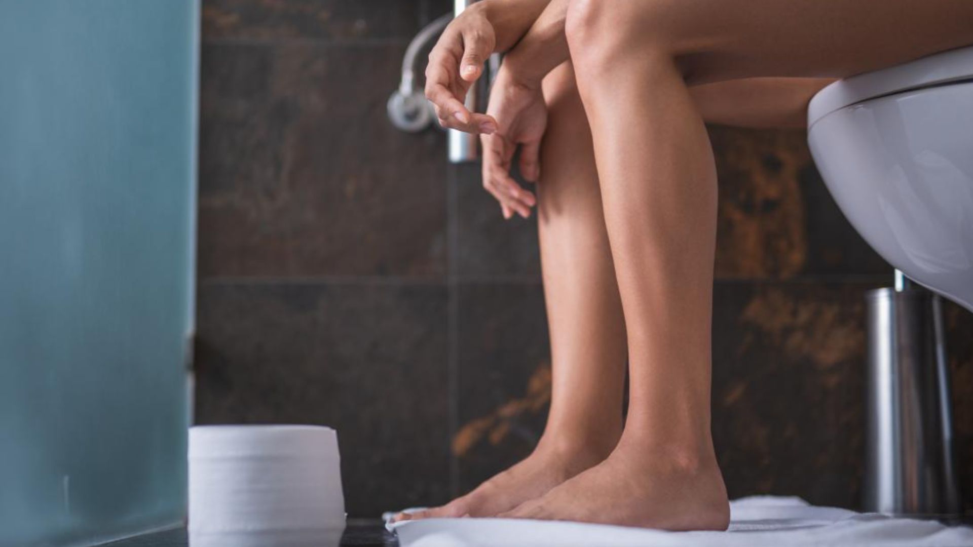 Person Sitting On Toilet With Naked Legs