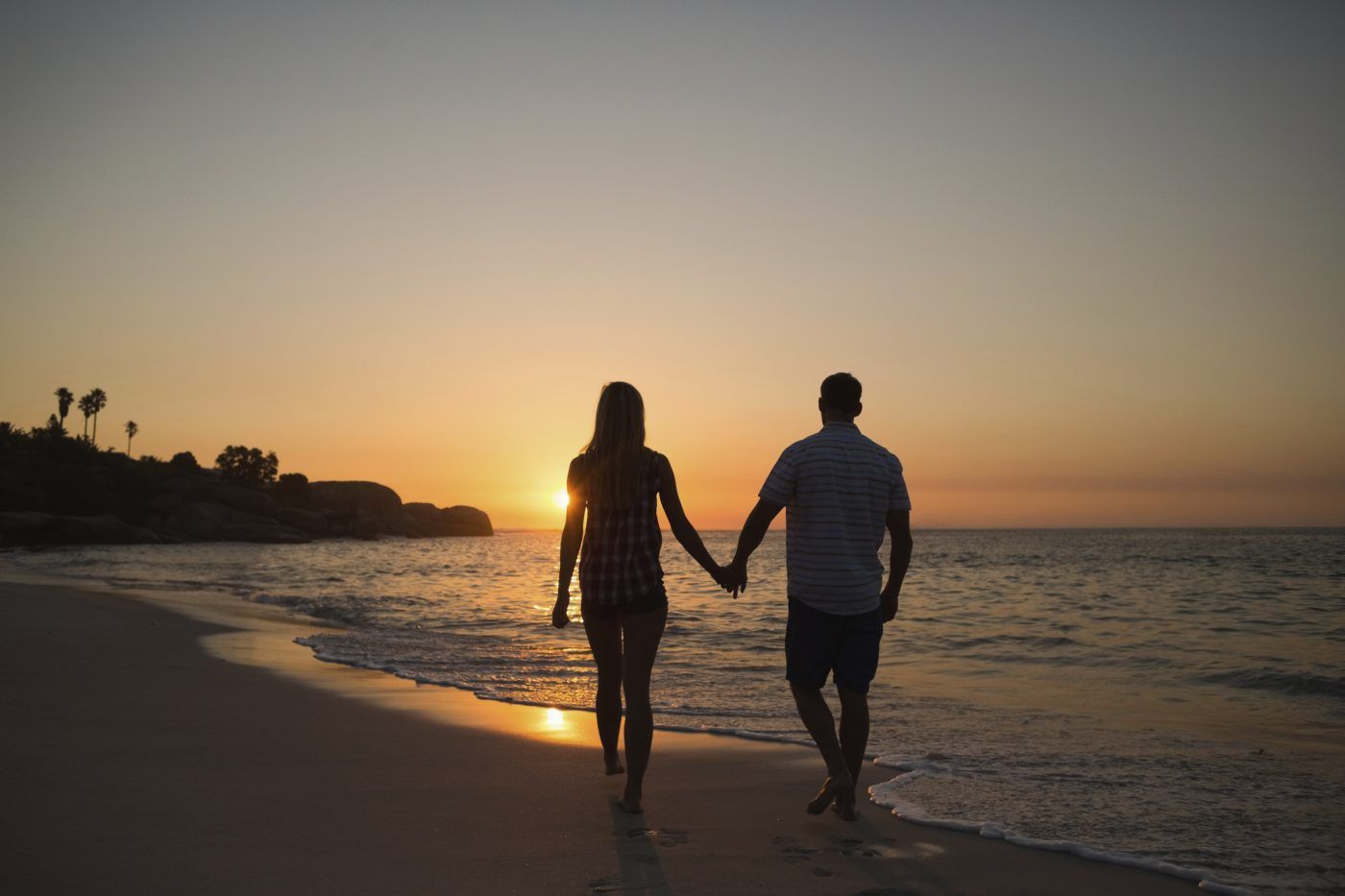 A couple holding hands in the beach while looking at the sunset