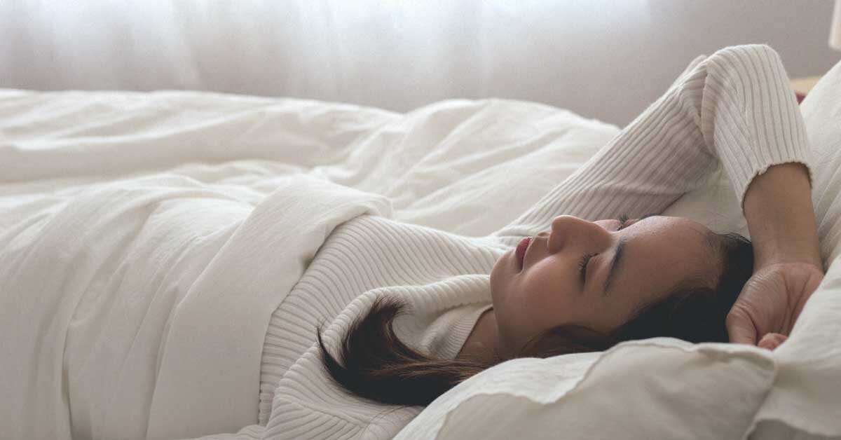 A woman wearing white long sleeves sleeping in a bed