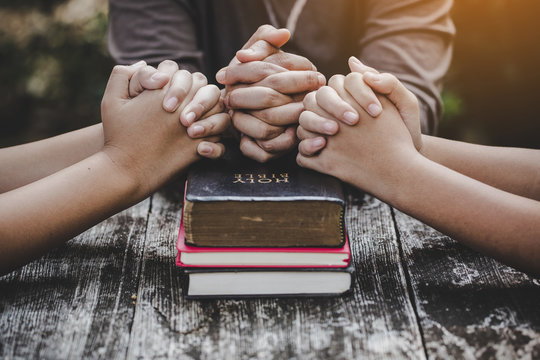 Group of 3 people praying with bibles beneath their hands