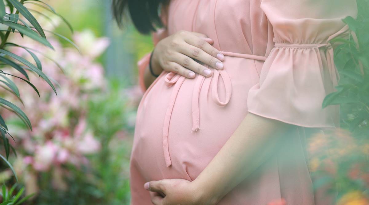 A pregnant holding her womb while wearing a pink dress in a garden
