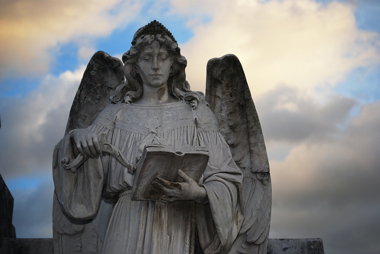 Stone Sculpture of an Angel with a Book against Clouded Sky